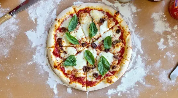 Pizza Margherita fraîchement sortie du four, avec son fromage fondant, ses olives et son basilic. Le temps de cuisson pizza four 250°C est parfait.