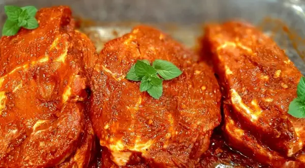 Karkówka na grilla w aromatycznej marynacie, gotowa do pieczenia. Liście mięty dodają świeżości.