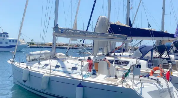 Barca a vela bianca ormeggiata, con scritte "17 FIRST" e "Finistère". Dettagli tecnici e mare calmo.