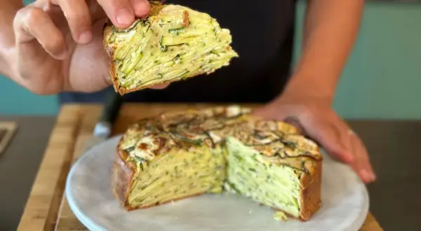 Une main tient une part d'un gâteau aux courgettes, révélant ses fines couches. Ce délice est presque invisible aux courgettes, tant elles sont bien intégrées.