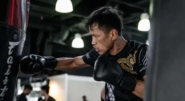 A boxer practices his form, throwing a punch at a heavy bag. His focus is intense as he trains.