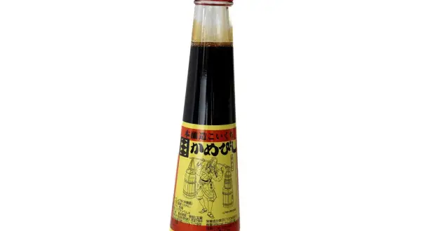 En flaska mörk sojasås med en röd kork. Etiketten visar en figur som bär korgar, vilket antyder att soja kan bli gammal och utveckla smak.