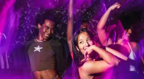 Giovani ballano al ritmo della musica techno in discoteca, immersi in luci viola e movimento.