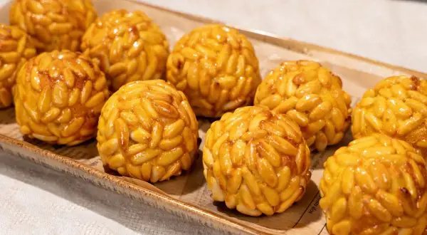 Panellets de boniato cubiertos de piñones dorados, presentados en una bandeja rústica.