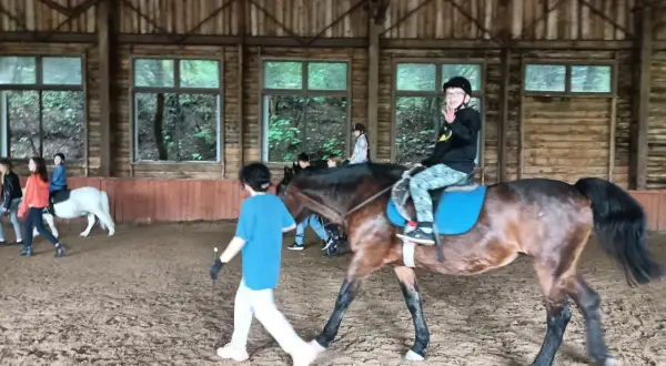 W stajni Black Horse Team Gdańsk, w owczarni, chłopiec na koniu macha do widza, a obok niego idzie instruktorka.