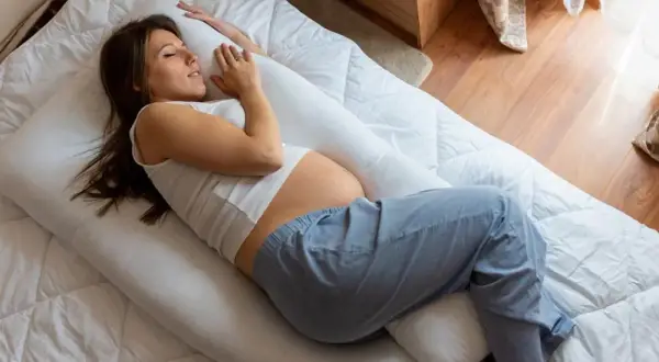 Une femme enceinte, en plein début de grossesse, peine à trouver le sommeil malgré un coussin de maternité.