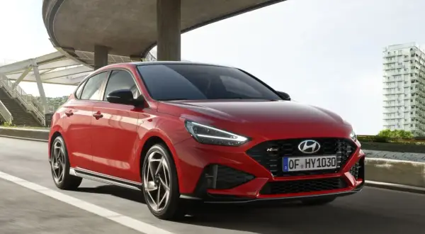 Czerwony Hyundai i30 hatchback N Line w ruchu miejskim, z nowoczesną architekturą w tle.