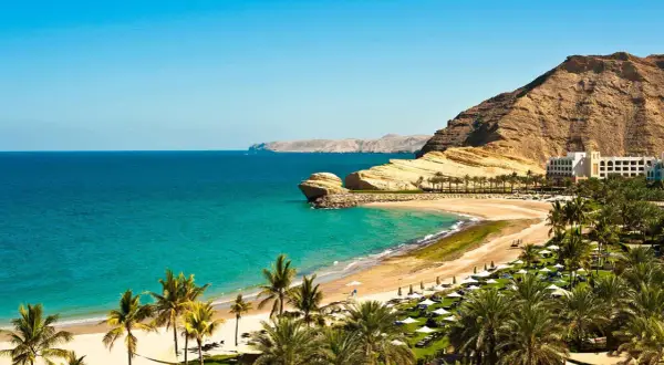 Traumhafte Bucht mit Palmen, Sandstrand und Felsen. Ein Hotel am Hang. Perfekt für Oman Reisetipps.