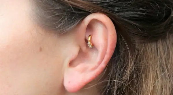 Złoty kolczyk w uchu, ozdobiony cyrkoniami, stanowi subtelny akcent. Ten rook piercing dodaje elegancji.