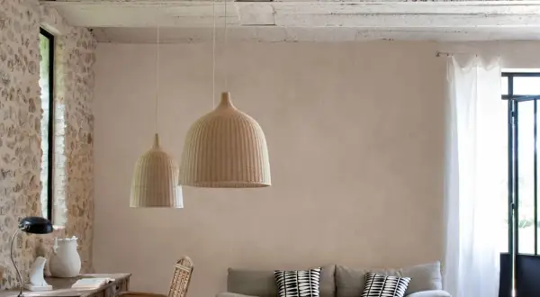 Un salon lumineux avec un mur en enduit mur interieur texturé, des suspensions en rotin, un canapé et des meubles en bois.
