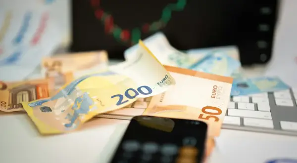 Euro banknoty na klawiaturze, telefon i wykres giełdowy sugerują inwestowanie w waluty.