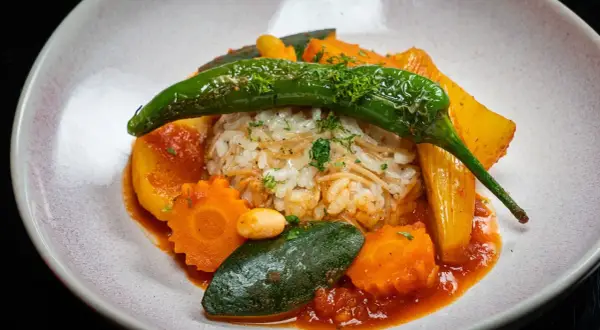 Herzhaftes Reisgericht mit viel Gemüse, darunter Karotten, Zucchini und eine grüne Chilischote, serviert in einer roten Sauce.