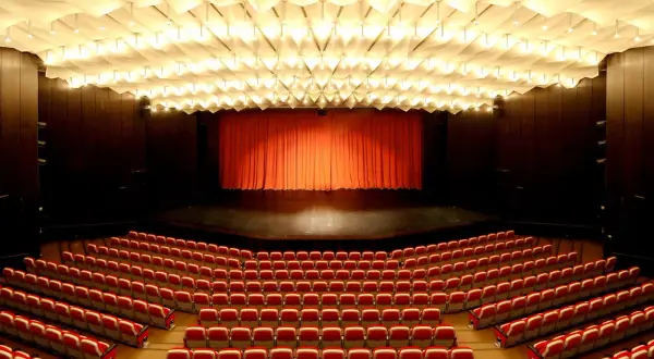 Leere rote Sitze im **Theater und Konzerthaus Solingen** warten auf Besucher. Die Bühne ist mit einem roten Vorhang verdeckt.