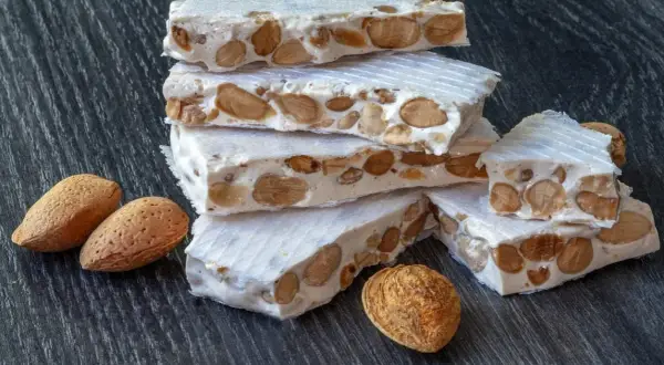 Barras de turrón, un dulce tradicional español, apiladas con almendras enteras. ¿Qué es nougat? Es este delicioso manjar.