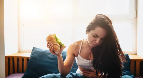 Donna con mal di stomaco tiene un panino, pensando cosa mangiare dopo aver vomitato.