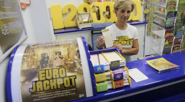 Kobieta w koszulce Eurojackpot trzyma kupon na tle stoiska z grami losowymi.