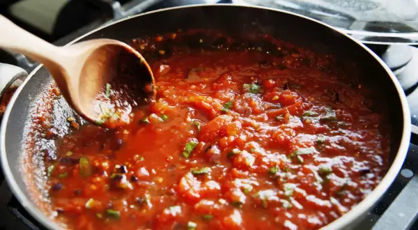 En träsked rör i en bubblande tomatsås i en stekpanna. Perfekt för ett enkelt tomatsås recept.