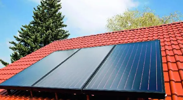 Montaż kolektorów słonecznych na czerwonym dachu. Trzy panele zbierają energię słoneczną, otoczone zielenią i błękitnym niebem.