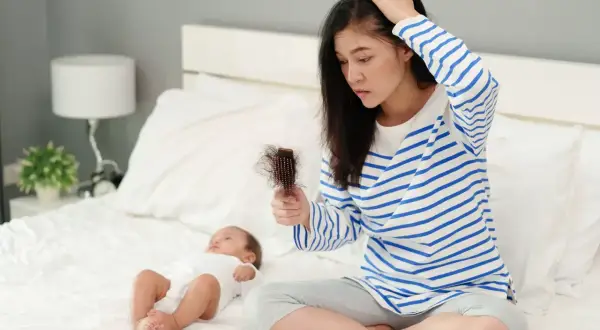 Maman inquiète par la chute de cheveux post-allaitement, cherchant un traitement naturel. Bébé dort paisiblement à côté.