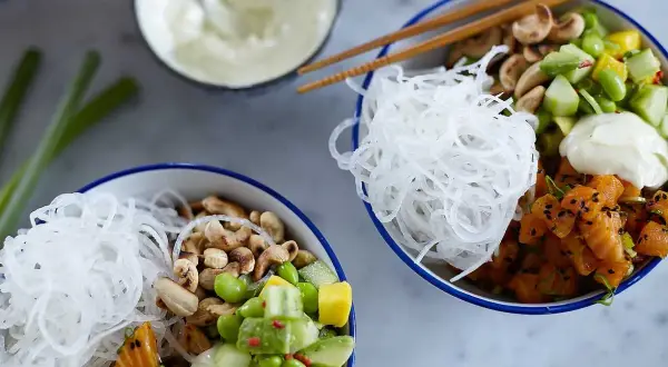 Två färgglada pokebowls med lax, grönsaker, nötter och risnudlar. Ett perfekt pokebowl recept för en hälsosam lunch.