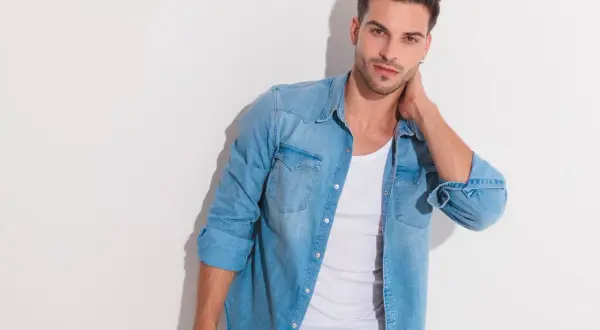 Junger Mann mit lässigem Look: blaues Jeanshemd über einem weißen Unterhemd unter T-Shirt.