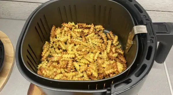 Chrupiące, pofalowane frytki ziemniaczane w koszu frytkownicy beztłuszczowej.