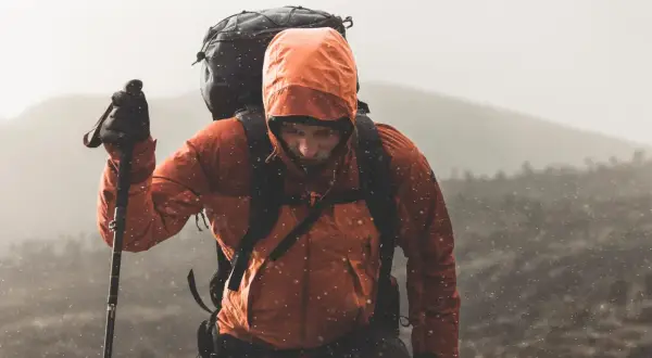 Turysta w pomarańczowej kurtce z kapturem i plecakiem wspina się po górach. Deszczowe Tatry szlaki na deszczowe dni nie straszne.