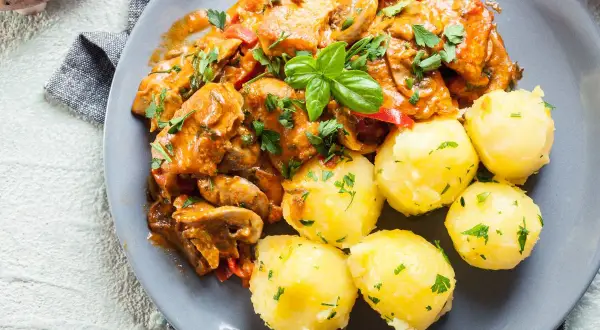 Pyszny gulasz z indyka z pieczarkami i papryką, podany z kluskami śląskimi posypanymi natką pietruszki.