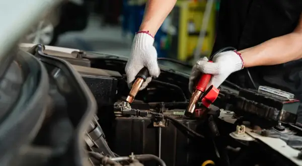Manos enguantadas conectando cables a la batería de un coche. Es hora de desconectar la batería del coche para un mantenimiento seguro.