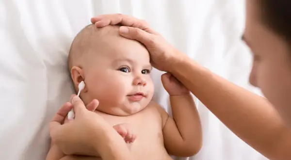 Delikatne czyszczenie uszu niemowlaka. Mama ostrożnie używa patyczka higienicznego, by zadbać o higienę maluszka.