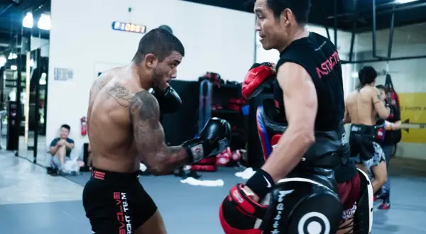 Boxers train in a gym. One boxer throws a punch, possibly an uppercut, as the other defends with pads.