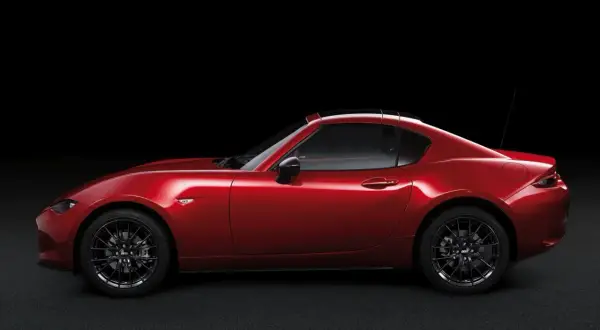Czerwona Mazda MX-5 RF targa z czarnym dachem, zaparkowana na ciemnym tle.