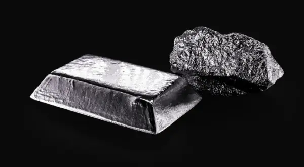 Sztabka i bryła platyny, najdroższego metalu na świecie, lśnią na czarnym tle.
