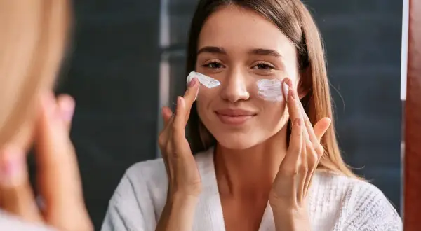 Kobieta w białym szlafroku nakłada kremy spf na twarz, dbając o ochronę skóry przed słońcem.