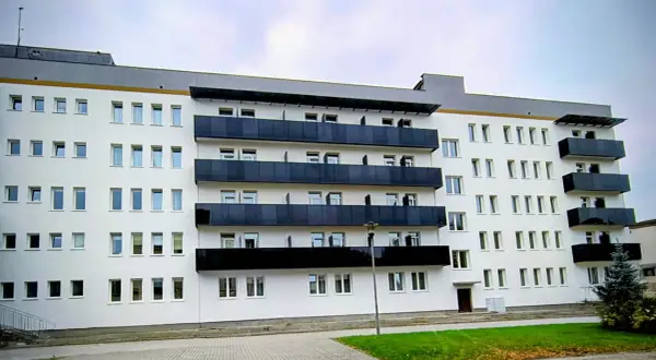 Nowoczesny budynek sanatorium uzdrowiskowego z białymi ścianami i czarnymi balkonami. W tle błękitne niebo.