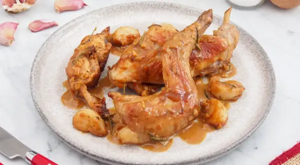 Plato de conejo al ajillo con trozos de ajo y romero. Una delicia para aprender cómo hacer conejo al ajillo.