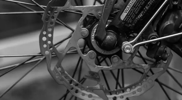 Zbliżenie na tarczę hamulcową i szprychy roweru. Widoczny mechanizm szybkiego zwalniania Shimano i ostrzeżenie. RWD.