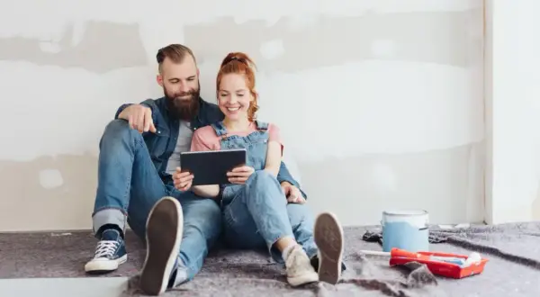Para uśmiecha się, patrząc na tablet, siedząc na podłodze w trakcie remontu.