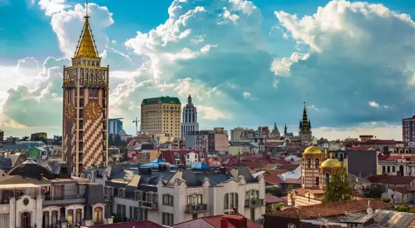 Widok na stolicę Adżarii, Batumi, z charakterystyczną wieżą zegarową i złotymi kopułami cerkwi pod błękitnym, chmurnym niebem.