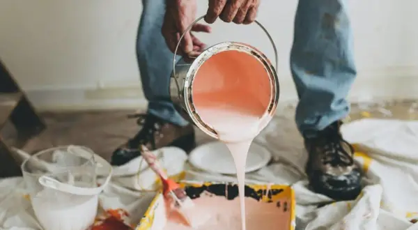 Mani versano pittura rosa da una latta in una vaschetta per rulli. Impara come diluire la pittura per un lavoro perfetto.