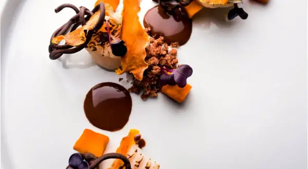 Postre de autor con chocolate, naranja y flores moradas. Una obra de arte culinaria que promete una experiencia gastronómica inolvidable.