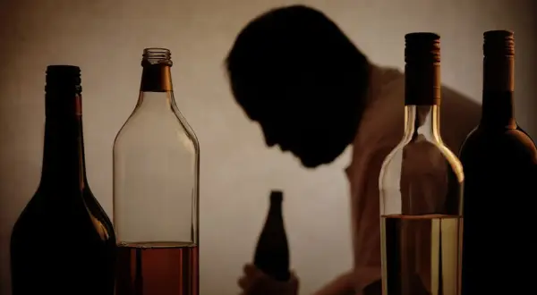 Flera flaskor alkohol framför en person i silhuett. Bilden illustrerar utmaningar med alkohol och arbetsgivarens rehabiliteringsansvar.