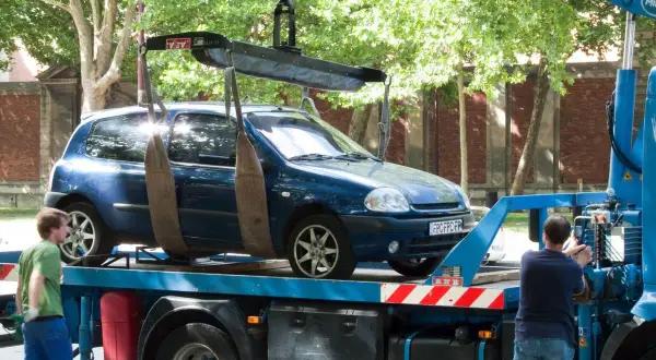 Une dépanneuse charge une voiture bleue. Si vous vous demandez comment savoir si ma voiture est à la fourrière, regardez si elle disparaît de là où vous l'avez garée.