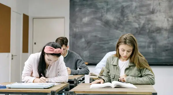 Uczniowie skupieni na zadaniach. Dziewczyna pisze, druga czyta. W tle tablica. Kiedy skończą, będą wiedzieć, jak budowa future perfect simple.