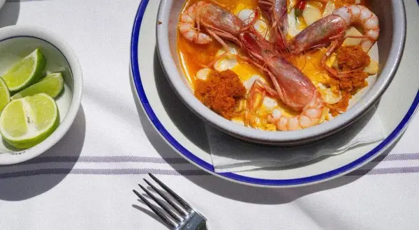 Un plato de gambas en salsa, preparado por un chef del mar, con gajos de lima al lado.