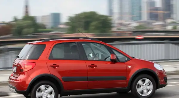 Czerwony Suzuki SX4 w ruchu miejskim. Wiele osób chwali ten model, a jego opinie są pozytywne.