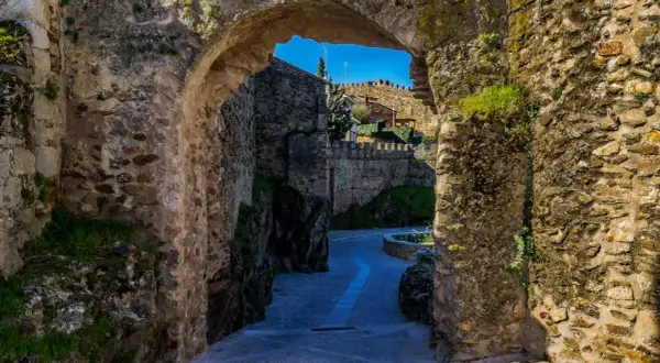 Un pasaje de piedra antigua nos lleva a descubrir lugares secretos de la Sierra de Madrid, con un camino empedrado y murallas que evocan historia.