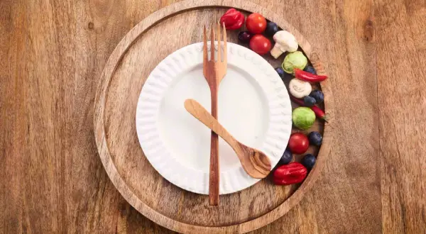Ein leeres Teller mit Holzbesteck und bunte Gemüse-Beeren-Deko. Bereit für 36 Stunden Fasten.