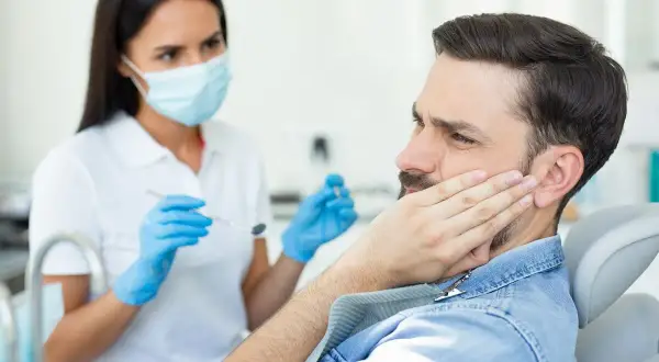 Mężczyzna z bólem policzka u dentysty, który bada jego dziąsła. Może to być objaw pogłębiających się kieszonki dziąsłowe.