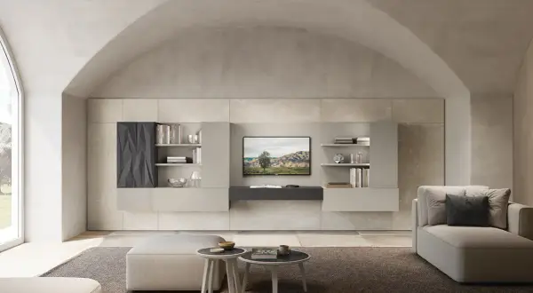Soggiorno moderno con divano, pouf e parete attrezzata. La **casa color sabbia** è illuminata da un grande lucernario ad arco.